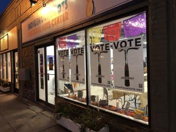 Indigenous Roots Cultural Arts center storefront at night with Vote posters