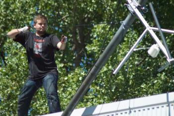 Photo of Will Floyd on roof holding wire attached to antenna pole.